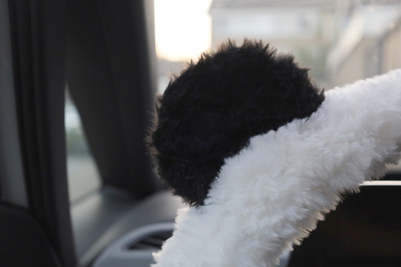May include: Black and white fuzzy steering wheel cover with a panda bear design.