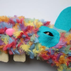 Puede incluir: Un peluche de piel sint&eacute;tica multicolor en tonos azul, amarillo, naranja y rosa. Tiene una nariz de pl&aacute;stico rosa brillante, dos dientes de fieltro color crema y un parche de fieltro turquesa en el ojo con pupila negra y una oreja turquesa.