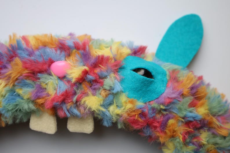 Puede incluir: Un peluche de piel sint&eacute;tica multicolor en tonos azul, amarillo, naranja y rosa. Tiene una nariz de pl&aacute;stico rosa brillante, dos dientes de fieltro color crema y un parche de fieltro turquesa en el ojo con pupila negra y una oreja turquesa.