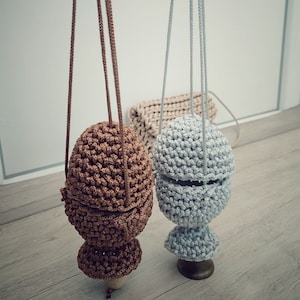 May include: Two crocheted hanging pouches, one brown and one grey, with a crocheted bag in the background.