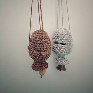 May include: Two hanging, crocheted mushroom-shaped objects. One is brown with a wooden bead, the other is gray with a brass base. Both have a string for hanging and a textured, rounded design.