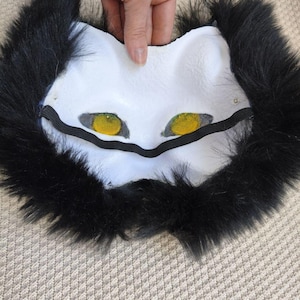Peut inclure: Un masque en forme d'animal blanc dot&eacute; de mailles jaunes vives sur les yeux et d'une &eacute;paisse bordure en fausse fourrure noire. Le masque comprend une sangle &eacute;lastique noire fix&eacute;e au niveau des yeux pour le maintenir en place.