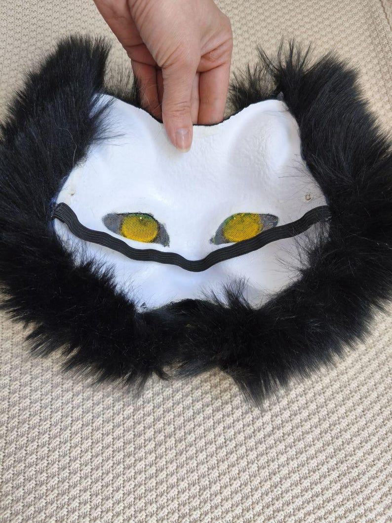 Peut inclure: Un masque en forme d'animal blanc dot&eacute; de mailles jaunes vives sur les yeux et d'une &eacute;paisse bordure en fausse fourrure noire. Le masque comprend une sangle &eacute;lastique noire fix&eacute;e au niveau des yeux pour le maintenir en place.