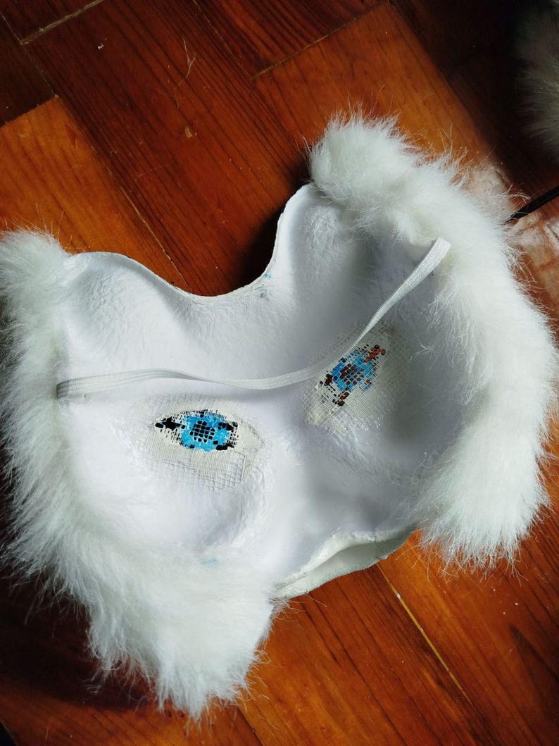 Pu&ograve; includere: Una maschera bianca con un bordo in pelliccia sintetica bianca lunga e soffice. L'interno della maschera &egrave; bianco e presenta due aperture per gli occhi coperte da un tessuto a rete blu e nero. Un sottile cinturino elastico bianco &egrave; fissato.