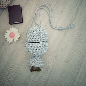 May include: A gray crocheted drawstring bag with a round bottom and a long cord handle.