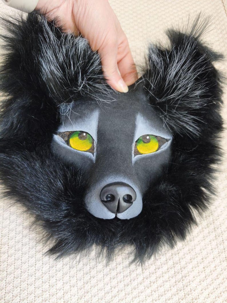 Peut inclure: Un masque de loup noir avec de la fausse fourrure longue et sombre, des oreilles pointues aux pointes argent&eacute;es et des yeux en maille jaune vif. Le museau est sculpt&eacute; avec une finition noire mate lisse et des nuances grises autour des yeux.