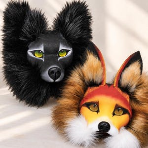 May include: Two animal masks featuring faux fur. One mask is black with bright green eyes and pointed ears. The second mask is orange, red, and white with yellow eyes and pointed ears. Both masks have a sculpted snout and a black nose.