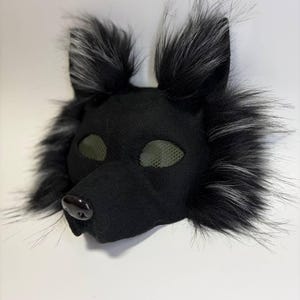 Peut inclure: Un masque de loup noir avec des détails en fausse fourrure. Le masque présente un nez sombre, des recouvrements d'yeux en filet et de la fausse fourrure noire et grise autour des oreilles et du visage. Le masque est conçu pour être porté.