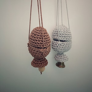 May include: Two crocheted hanging ornaments, one brown and one grey. The brown ornament is round with a wooden bead at the bottom. The grey ornament has a more intricate design with a rounded top and a pointed bottom.