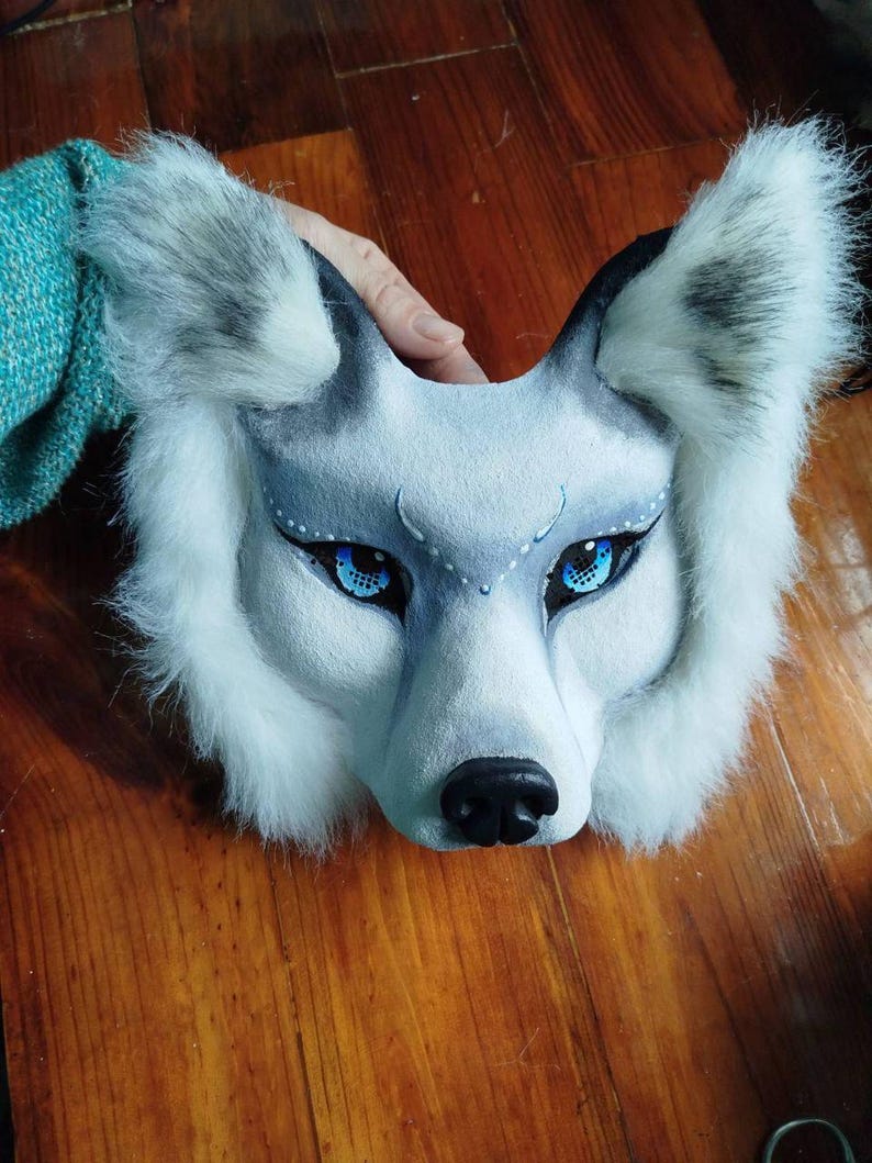 Pu&ograve; includere: Una maschera da lupo con pelliccia sintetica bianca e grigia, occhi blu brillante con eyeliner nero e puntini bianchi sopra gli occhi. La maschera presenta un muso scolpito con un naso nero e orecchie a punta con le estremit&agrave; grigie.