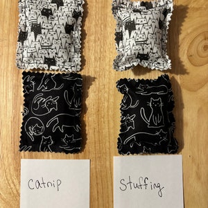 May include: Two black and white cat-patterned fabric pouches with a white label that says "catnip" and a white label that says "stuffing".
