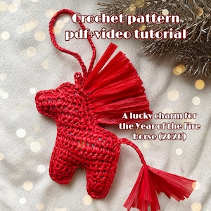 Könnte beinhalten: Roter Häkelpferdschmuck mit Mähne und Schweif aus Bast. Der Text auf dem Bild lautet "Crochet pattern pdf+video tutorial" und "A lucky charm for the Year of the Fire Horse (2026)".