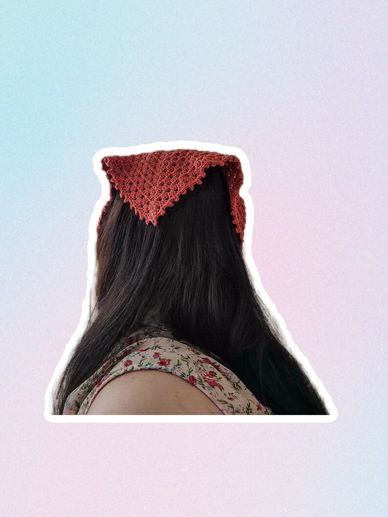 Op de afbeelding: Een vrouw met lang donker haar die een terracotta geh&auml;kelde bandana om haar hoofd draagt.