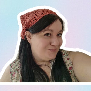 Op de afbeelding: Een vrouw met lang donker haar die een gehaakt hoofdband draagt in een verbrand oranje kleur. Ze draagt een top met bloemenprint zonder mouwen.