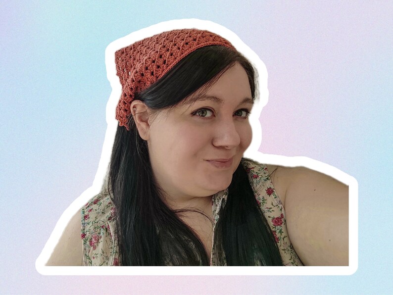Op de afbeelding: Een vrouw met lang donker haar die een gehaakt hoofdband draagt in een verbrand oranje kleur. Ze draagt een top met bloemenprint zonder mouwen.
