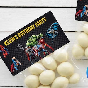 Puede incluir: Dos bolsas transparentes llenas de caramelos blancos, cada una con una etiqueta rectangular negra que dice "KEVIN'S BIRTHDAY PARTY" en amarillo. Las etiquetas presentan superhéroes de cómics como Spider-Man, Superman y Hulk.