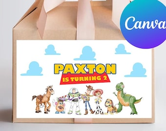 Puede incluir: Una caja de regalo marrón con una cinta rosa claro. La parte delantera de la caja presenta un rectángulo blanco con el texto "PAXTON IS TURNING 2" y personajes de dibujos animados. También hay nubes azules.
