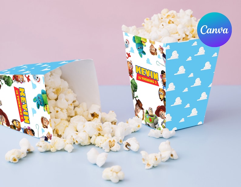 Op de afbeelding: Twee popcornbakjes, &eacute;&eacute;n rechtop en &eacute;&eacute;n omgekiept, gevuld met popcorn. De bakjes zijn lichtblauw met witte wolken en karakterillustraties. De tekst "KEVIN IS TURNING 3" staat op de voorkant.