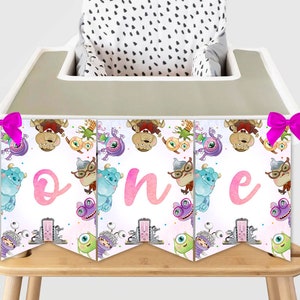 May include: A colourful banner featuring cartoon monsters and the word "one" in pink script. The banner is attached to a high chair with pink bows. The high chair has a black and white polka dot seat cover.