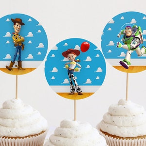May include: Three cupcake toppers featuring characters from the animated film Toy Story. Woody, in a cowboy hat and outfit, Jessie with a red balloon, and Buzz Lightyear in a space suit, are set against a blue sky background.
