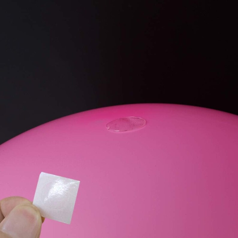 May include: A close-up of a pink balloon with a clear adhesive patch on the surface. A white adhesive patch is held in a hand, ready to be applied.