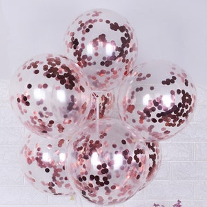 May include: A cluster of six clear balloons filled with rose gold confetti. The balloons are tied together and ready for a party.