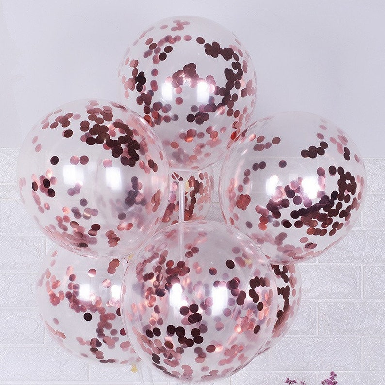 May include: A cluster of six clear balloons filled with rose gold confetti. The balloons are tied together and ready for a party.
