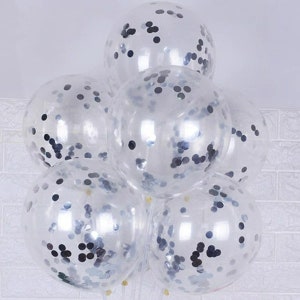 May include: A cluster of clear balloons with black confetti inside. The balloons are tied together and are floating in the air.