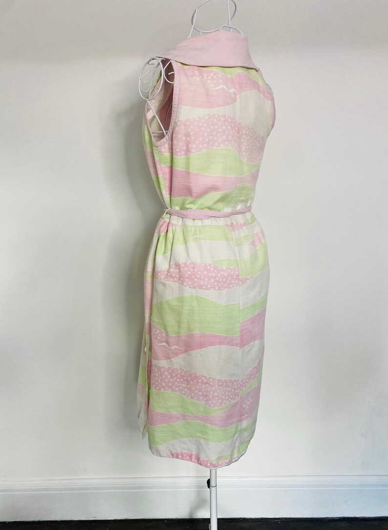 Może przedstawiać: R&oacute;żowa i zielona sukienka bez rękaw&oacute;w z białym tłem i wzorem w kropki. Sukienka ma r&oacute;żową wstążkę zawiązaną w talii.