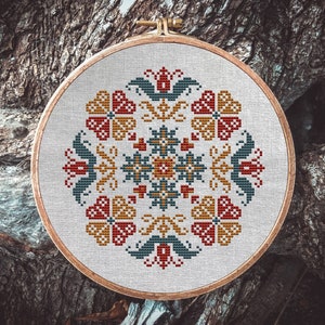 May include: A circular embroidery hoop with a white fabric background and a colorful cross-stitch design featuring red, yellow, and blue flowers. The design is symmetrical and has a geometric pattern.