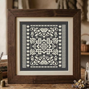 May include: A framed cross-stitch embroidery featuring a dark gray background with a white geometric pattern. The design includes a central square motif, floral elements, heart shapes, and vertical Greek key borders. The text LesMagicArtPatterns is visible.