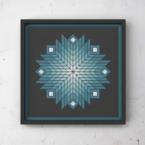 Pode incluir: Obra de arte em ponto cruz, emoldurada, com um design geométrico em tons de azul e branco, assemelhando-se a uma estrela. A obra está sobre um fundo cinza escuro e emoldurada em uma moldura quadrada preta, criando uma estética moderna.