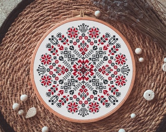 May include: A round embroidery hoop with a white fabric background and a red, black, and white geometric pattern. The pattern is a traditional folk design with a circular shape.