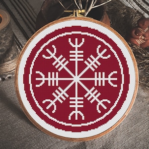 May include: A red and white embroidered hoop art piece featuring a white Vegvisir symbol on a red background.