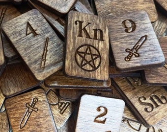 May include: A close-up of a pile of wooden tiles with various numbers, symbols, and letters, including "Kn" and a pentagram. The tiles are stained a dark brown color and have a rustic appearance.