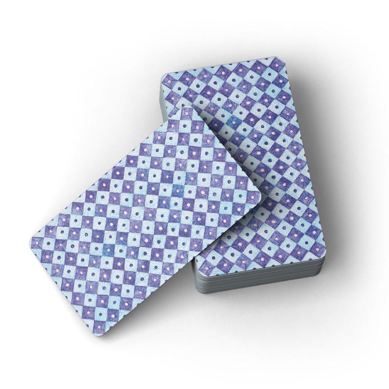 Puede incluir: Una baraja de cartas con un patr&oacute;n de cuadros azules y morados. Las cartas est&aacute;n dispuestas en una pila con una carta extendida. Cada carta tiene un peque&ntilde;o punto blanco en el centro de cada cuadrado.