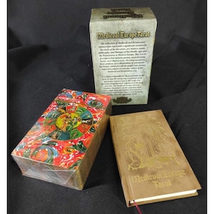 May include: A Medieval Europe Tarot card set with a box and a book. The box has a colorful, patterned design, while the book and box are tan with gold lettering. The box has text that describes the tarot cards.