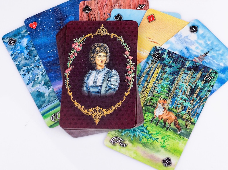 Op de afbeelding: Een tarotkaartspel met diverse aquarel illustraties. De centrale kaart toont een portret in een decoratief kader. Andere kaarten tonen sc&egrave;nes uit de natuur, waaronder een vos, en hemellandschappen. De kaarten zijn gerangschikt op een wit oppervlak.