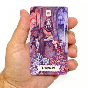 K&ouml;nnte beinhalten: Eine Tarotkarten-Illustration der M&auml;&szlig;igkeit, der 14. Karte der Gro&szlig;en Arkana. Die Karte zeigt eine Person in einer Robe, die Fl&uuml;ssigkeit von einem Becher in einen anderen gie&szlig;t, mit einem Hintergrund aus einem gotischen Schloss und einem Vollmond. Die Karte ist von roten und blauen Blumen umgeben.
