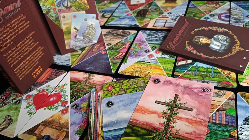 Op de afbeelding: Een Lenormand solitaire kaartspel met een bruine doos en kaarten met aquarel illustraties. De kaarten tonen verschillende afbeeldingen, waaronder een hart, een kruis en landschappen. De doos heeft de naam "Lenormand" erop.