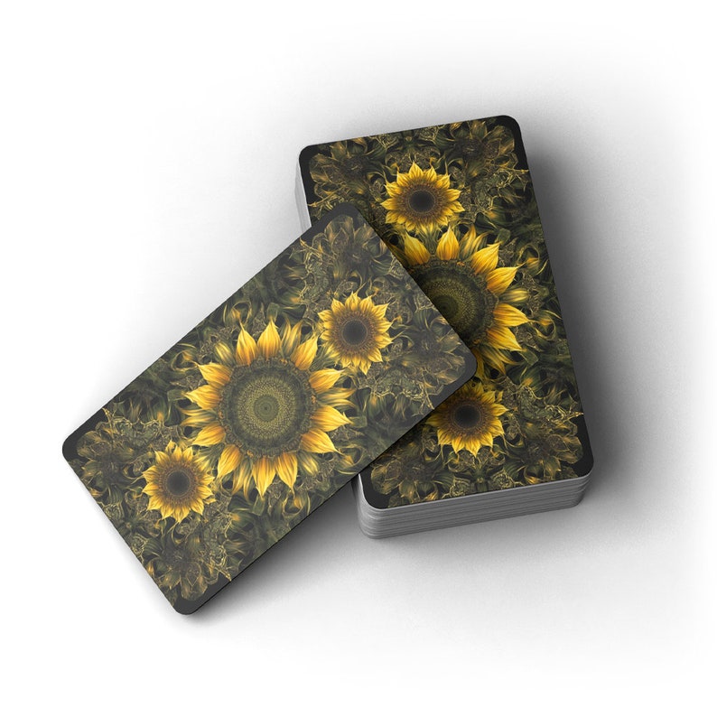 May include: A deck of rectangular cards with a sunflower design. The cards have a dark background with yellow sunflowers and detailed patterns. The deck is stacked with a few cards fanned out, displaying the floral artwork.