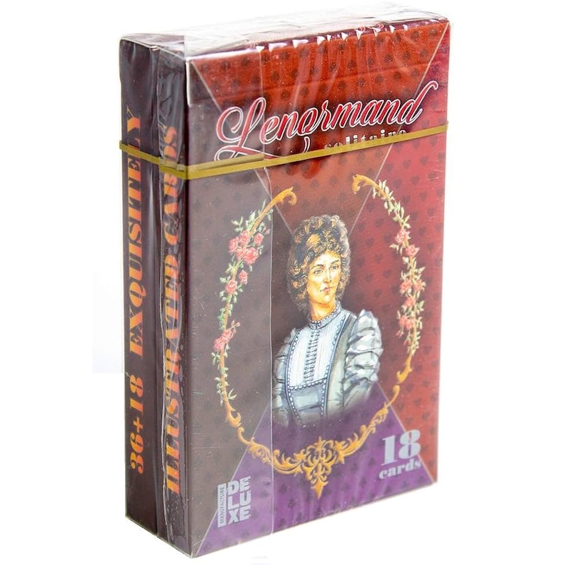 Op de afbeelding: Een kaartspel voor Lenormand solitaire in een doos. De doos is verpakt in transparant plastic en vastgezet met een gele elastiek. De doos toont een portret van een vrouw, bloemmotieven en de tekst "Lenormand solitaire" en "36+18 EXQUISITELY ILLUSTRATED CARDS".