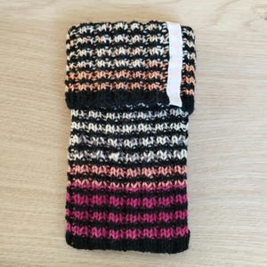 Könnte beinhalten: Ein gestrickter Beinstulpen in Schwarz, Rosa und Creme mit einem weißen Etikett.