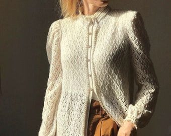 May include: A white crocheted cardigan with a button-up front and long sleeves. The cardigan has a delicate lace pattern and is worn over a brown skirt.