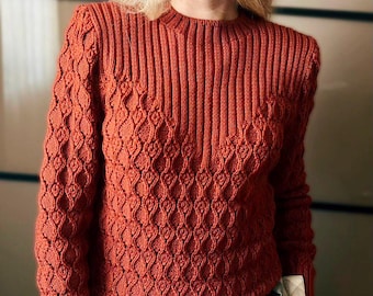 Puede incluir: Un suéter de punto color óxido con cuello redondo. Las mangas presentan un patrón de diamantes, mientras que el cuerpo tiene canalé vertical. El suéter está hecho de un material suave y texturizado, ideal para climas más frescos. Las mangas son largas.