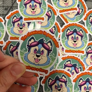 May include: A stack of colorful stickers featuring a cartoon blue wolf wearing goggles and a green background. The text on the stickers reads "The chemicals in pool water made me a furry".