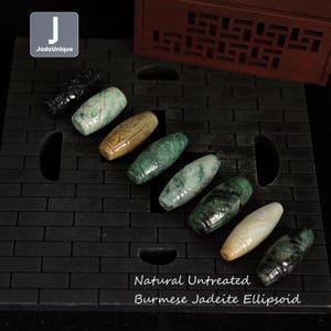 Può includere: Una collezione di otto perle ellissoidali di giadeite birmana naturale non trattata, in varie tonalità di verde e marrone. Le perle sono disposte su una superficie nera con il testo "Natural Untreated Burmese Jadeite Ellipsoid" sotto.