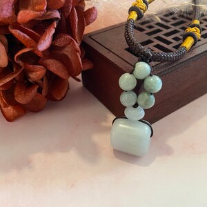 May include: A jade necklace with a rectangular pendant and round beads. The necklace is on a brown wooden box with a lattice design.