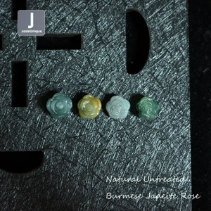 May include: Four natural, untreated Burmese jadeite rose beads in various shades of green, yellow, and white. The beads are arranged in a row on a dark grey textured surface. Natural Untreated Burmese Jadeite Rose.