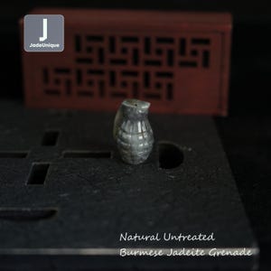 May include: Natural untreated Burmese Jadeite grenade pendant. The pendant is carved in the shape of a grenade and is a light gray color.